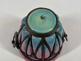 a colorful vase with a black handle on a white surface