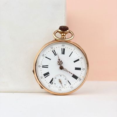 montre de poche en or avec des chiffres romains, posée sur un socle en marbre
