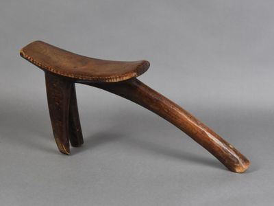 a small wooden stool with a curved seat on a gray surface