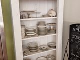une armoire blanche sur laquelle sont posées des assiettes et un tableau noir posé par terre