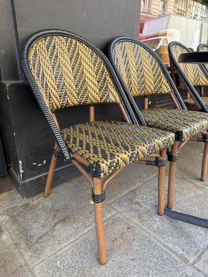 trois chaises en osier sont alignées contre un mur, sur un trottoir