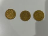 three gold coins sitting on top of a white table next to a shadow of a person