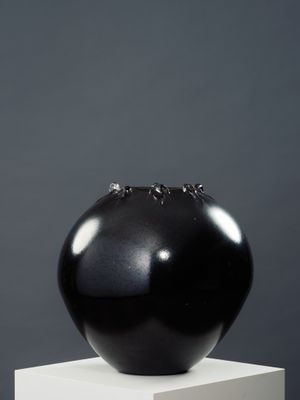 sculpture représentant un vase noir posé sur un socle blanc, sur fond gris