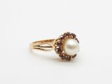 a close up of a ring with a pearl and garnets