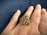 an image of a woman ' s hand holding a gold ring with green and red stones