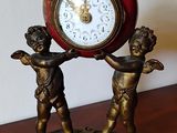 une horloge posée sur une table où se trouve une statue représentant deux enfants