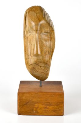 une photo d'une sculpture en bois représentant un visage, posée sur un socle en bois