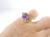 a woman ' s hand holding a purple and green ring