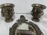 two silver vases sitting next to a mirror on a table