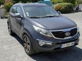La voiture grise est garée sur le parking, près des buissons.