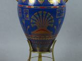un vase bleu posé sur un socle, muni d'une anse dorée