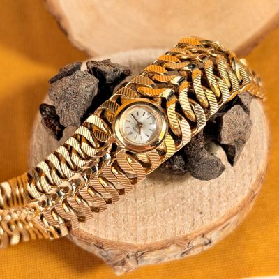 un bracelet en or avec une montre posée sur un morceau de bois