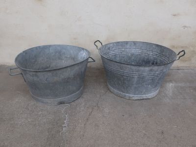 two metal buckets sitting next to each other on the ground