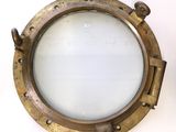 brass porthole mirror on a white wall with a white background