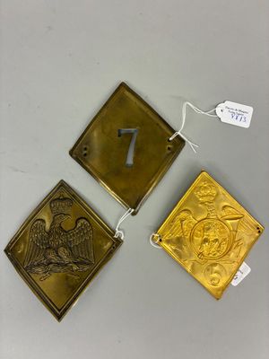 trois plaques et étiquettes en laiton posées sur une table, accompagnées d'étiquettes