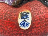 a red vase with blue writing on it sitting on a table