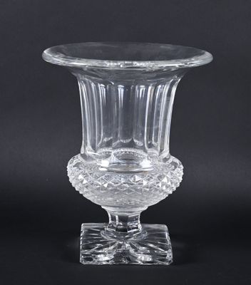 un vase en verre transparent posé sur un socle, sur fond noir