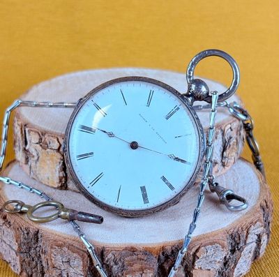 a silver pocket watch sitting on a piece of wood