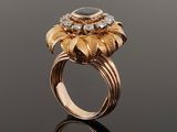 a close up of a gold ring with an oval stone surrounded by leaves