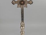 a silver cross on a stand with a red stone in the center
