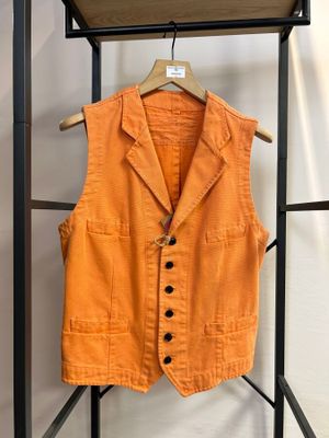 Un gilet orange est suspendu à un porte-vêtements devant un mur blanc.