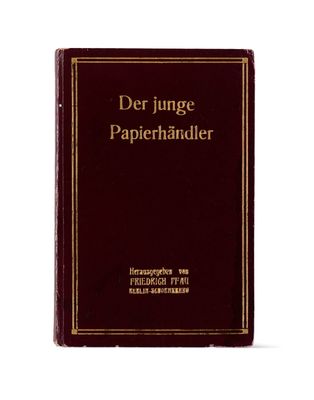 un livre rouge avec des lettres dorées posé sur une surface blanche