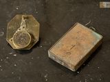 an old book sitting next to a small clock on top of a table