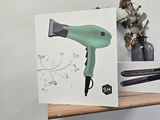 a green blow dryer sitting on a shelf next to a vase of flowers