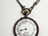 une montre de poche ancienne avec une chaîne, posée sur une surface blanche