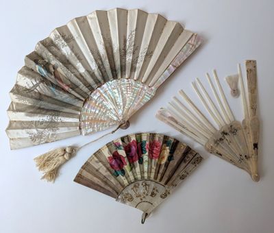 Plusieurs éventails anciens sont exposés sur une surface blanche