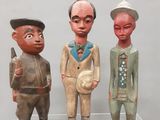trois figurines en bois représentant des hommes, posées sur une étagère transparente