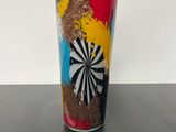 a colorful cup sitting on a table with a white wall in the background