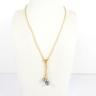 a gold necklace with a black pearl on a mannequin neck