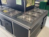 stainless steel counter top with four pans and a shelf of food