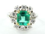 un gros plan d'une bague sertie d'une émeraude verte et de diamants, posée sur une surface blanche
