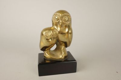 statue représentant un hibou en or tenant un bébé, posée sur un socle en marbre noir