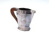 a silver pitcher with a wooden handle on a white surface