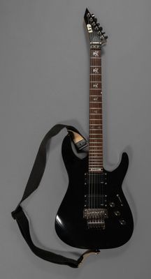 une guitare électrique à laquelle est accrochée une sangle au niveau du manche