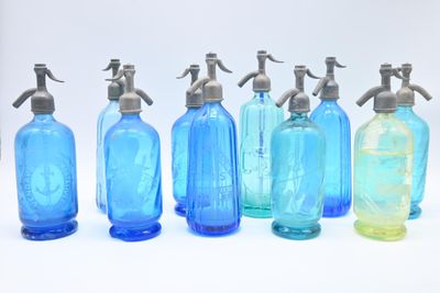 six bouteilles en verre bleues sont alignées sur une surface blanche