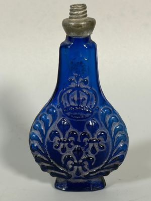 une bouteille en verre bleue avec un bouchon argenté, posée sur une surface blanche