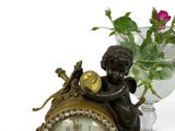 a clock with a little boy sitting on it next to a vase of flowers