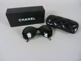 Lunettes de soleil Chanel et leur étui posés sur une surface blanche, avec une boîte noire