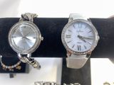 two watches and bracelets on display on a black stand