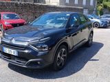 une voiture noire garée sur un parking près d'un mur de pierre