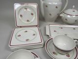 a white table with red and green dishes and cups and saucers