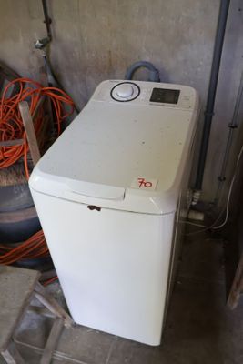 une machine à laver blanche posée dans un garage, à côté d'un tas de pneus