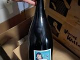 a woman holding a bottle of wine in front of a cardboard box