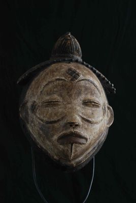 un vieux masque en bois accroché à un mur noir sur fond noir