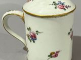 a white cup with a gold rim and a flower pattern on it