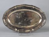 an oval silver plate on a stand on a gray background